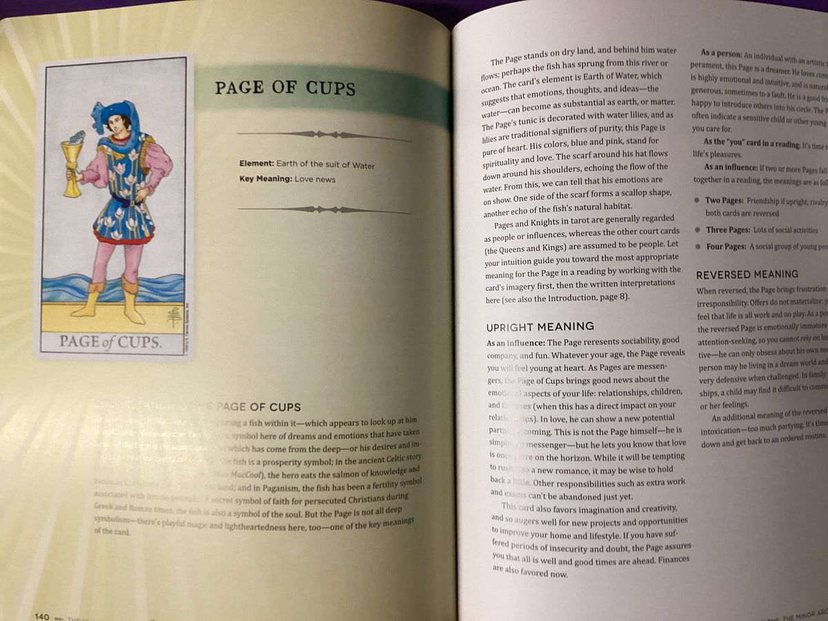 An open book showing two printed pages with text and a small illustration labeled 'PAGE OF CUPS' on the left page.