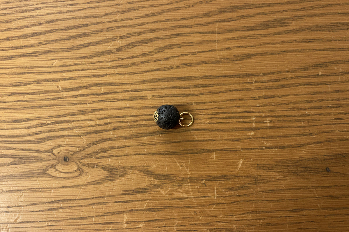 A small black spherical bead with gold lettering and a gold ring loop, placed on a scratched purple surface.